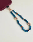 Close-up of Leah apatite phone charm with blue apatite beads, red accents, and gold evil eye charms attached to phone case