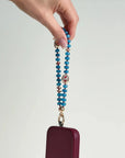 Leah apatite phone charm with evil eye charm attached to burgundy phone case, held in hand against a clean white background