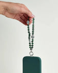 Leah phone charm in emerald quartz with silver evil eye charms attached to a green phone case, held against a white background