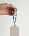 Mini Leah turquoise phone charm attached to a blush pink phone case, held in hand against a clean white background
