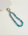 Mini Leah turquoise phone charm with blue beads, purple evil eye charms, and gold details attached to a blush pink phone case
