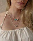 Noa silver turquoise quartz necklace layered with an evil eye pendant necklace on a white top, MyAleph We Are One Collection
