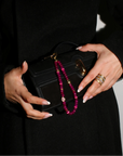 Leah Bag Charm held with a black clutch – A hand elegantly holding the amethyst quartz charm attached to a black clutch, showcasing its refined and sophisticated appeal.
