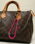 Stella Bag Charm attached to a luxury brown monogram handbag – The pink quartz charm clipped onto a brown leather designer bag, showing its versatile and stylish appeal.