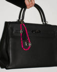 Stella Bag Charm attached to a black handbag – The pink quartz charm clipped onto a structured black handbag, adding a statement of confidence and sophistication.