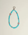 The Leah Bag Charm in Turquoise displayed against a neutral background, showcasing its faceted turquoise quartz beads, rhodium-plated silver Evil Eye charms, and pink accent dividers.