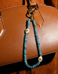 The Stella Bag Charm in Apatite elegantly draped over a handbag, showcasing its luxurious design with gold-plated accents, apatite quartz beads, and an Evil Eye charm for a stylish and protective touch.
