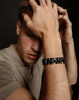 A man resting his hand on his head while wearing three David Bracelets in Black Rhodium, Gold, and Silver, emphasizing the contrast between the finishes and the understated, modern look.