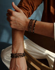 A man crossing his arms, styled with the David Bracelet in 18K Gold and the Ethan Wrap in 18K Gold, showcasing the contrast between the single bracelet and the wrap design for a bold, sophisticated look.