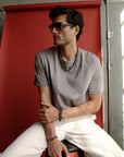 A man seated against a red backdrop, wearing the Ethan Wrap in Silver as a bracelet, styled casually with a relaxed, minimalist look.