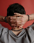 A man resting his head on his hands, wearing the Ethan Wrap in Silver as a bracelet and necklace, highlighting the wrap’s convertible style and layered look.