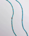 Turquoise beaded belly chain with gold accent beads and a central evil eye charm, laid out on a white background.
