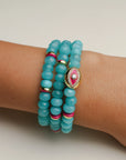 A set of three Leah turquoise bracelets worn on the wrist, featuring vibrant blue-green beads with pink and gold accents and a central eye charm for a playful and bold look.
