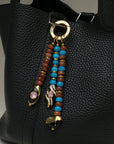 The Liora Bag Charm in Azure & Espresso attached to a black leather bag, adding an elegant and colorful accent.