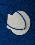 MyAleph Luna Cord Necklace in Azur with cobalt blue cord and silver evil eye pendant styled on seashell and blue textured background