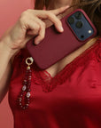 Mini Leah Ruby Quartz Phone Charm hanging from burgundy phone case styled with red lace top.