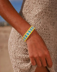 MyAleph Riviera Bracelet in Mykonos — turquoise and yellow evil eye talisman bracelet worn on wrist, styled with a cream knit summer dress at the beach.