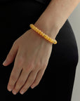 Tangerine quartz beaded bracelet with gold accents worn on wrist, vibrant orange gemstone jewelry styled with black outfit