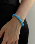 Azure blue quartz beaded bracelet with gold spacers worn on wrist, bright blue gemstone bracelet styled against black clothing