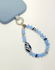 Mini Minou Aquamarine Quartz Phone Charm attached to a light blue phone case, featuring aqua-toned beads with a gold zebra evil eye charm.