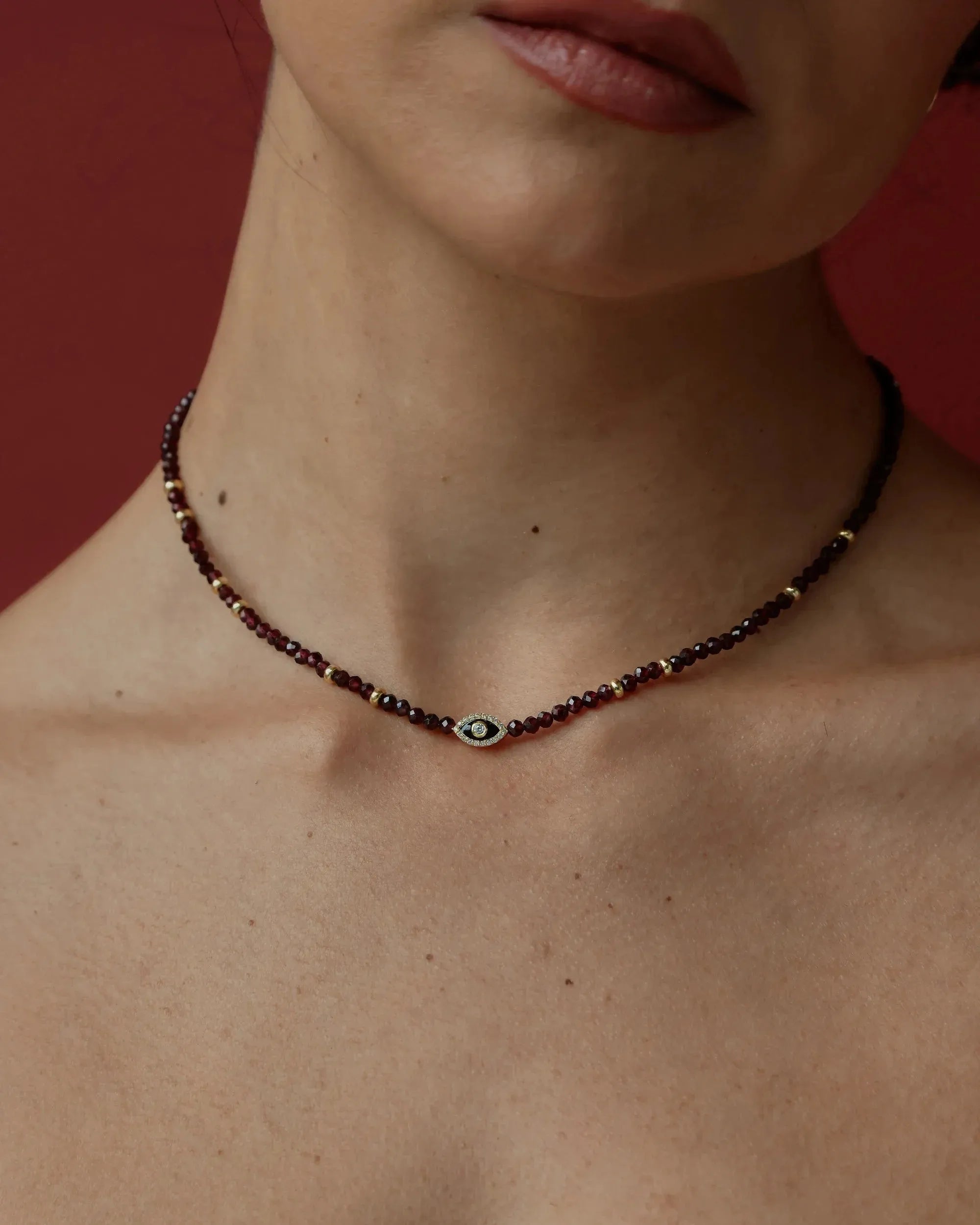 Necklace with a small evil eye charm worn by a person against a red background
