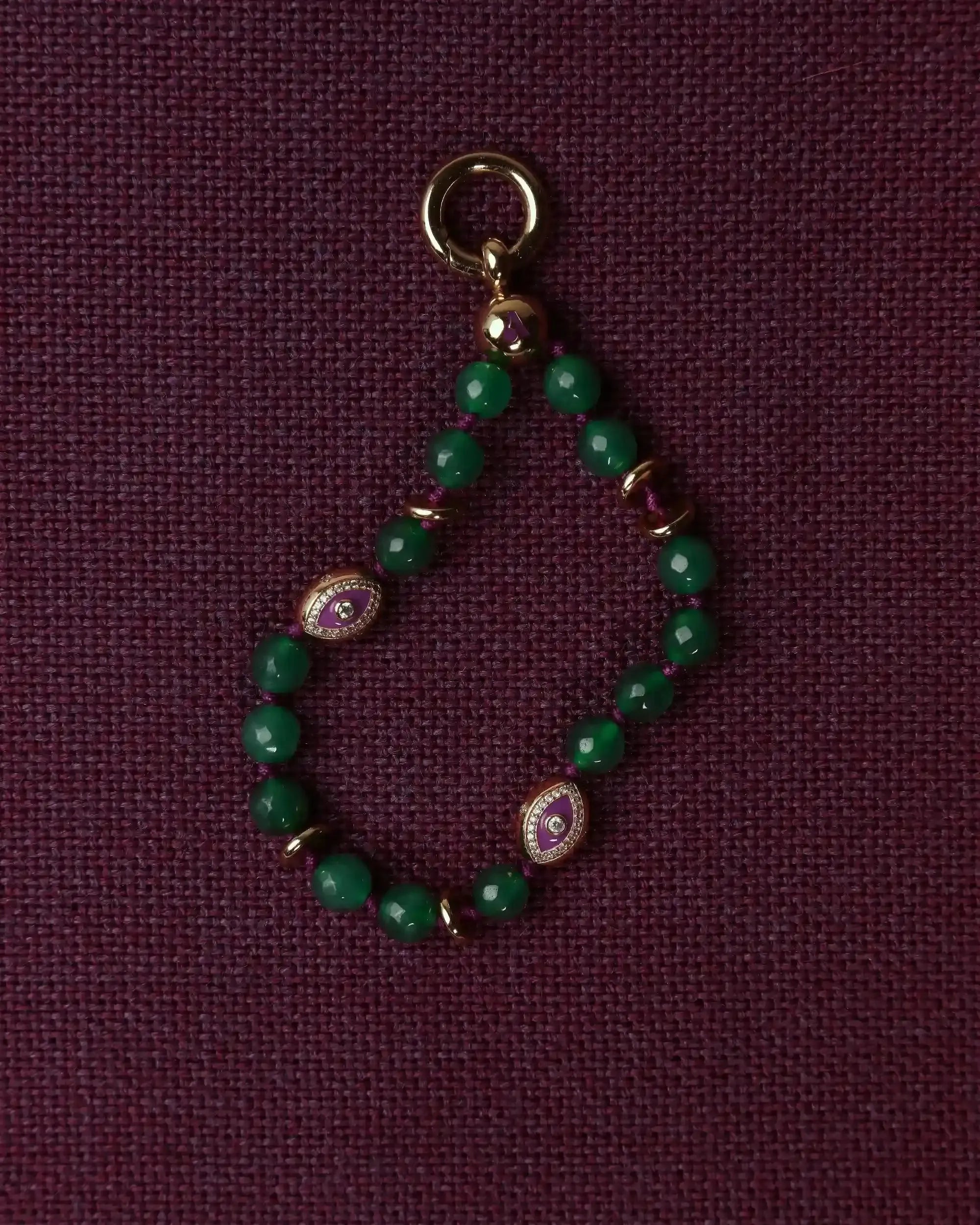 Green beaded charm with gold and purple accents on a dark purple background