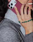 Person holding a phone with a pink case, wearing a green beaded bracelet.
