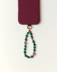 Green beaded phone charm with a purple heart pendant on a white background
