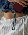 Leah apatite phone charm with evil eye charms hanging from burgundy phone case, styled with denim and striped shorts