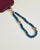 Close-up of Leah apatite phone charm with blue apatite beads, red accents, and gold evil eye charms attached to phone case