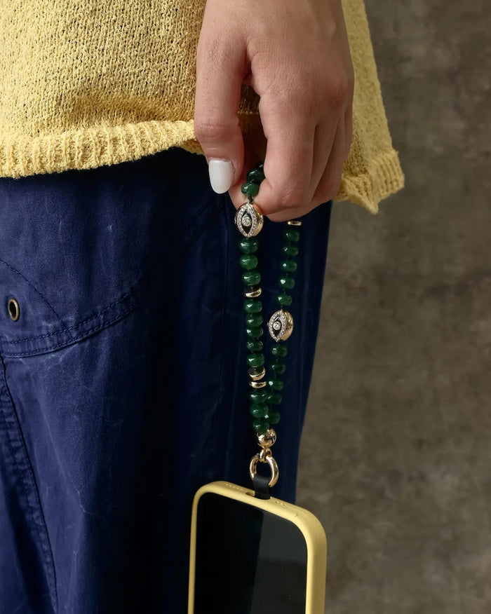 Leah emerald phone charm in gold with green gemstone beads and evil eye charms attached to a gold phone case