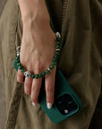 Leah phone charm in emerald quartz with silver evil eye wrapped around hand and attached to a green phone case