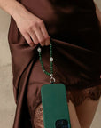 Leah phone charm in emerald quartz with silver evil eye attached to a green phone case, styled against a brown satin dress