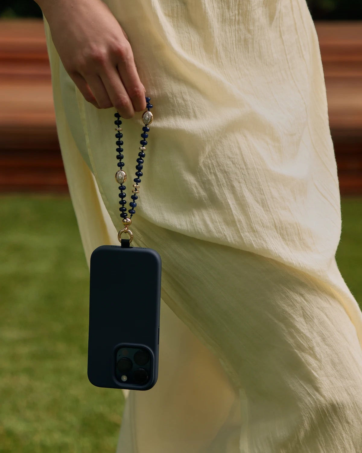 Leah sapphire phone charm with navy phone case held by hand against a flowing cream dress outdoors