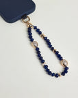 Close-up of Leah sapphire phone charm with deep blue beads, gold accents, and evil eye charms attached to a navy phone case