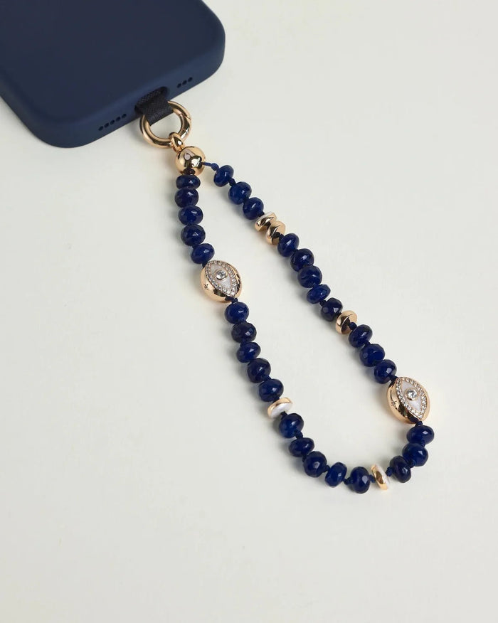 Close-up of Leah sapphire phone charm with deep blue beads, gold accents, and evil eye charms attached to a navy phone case