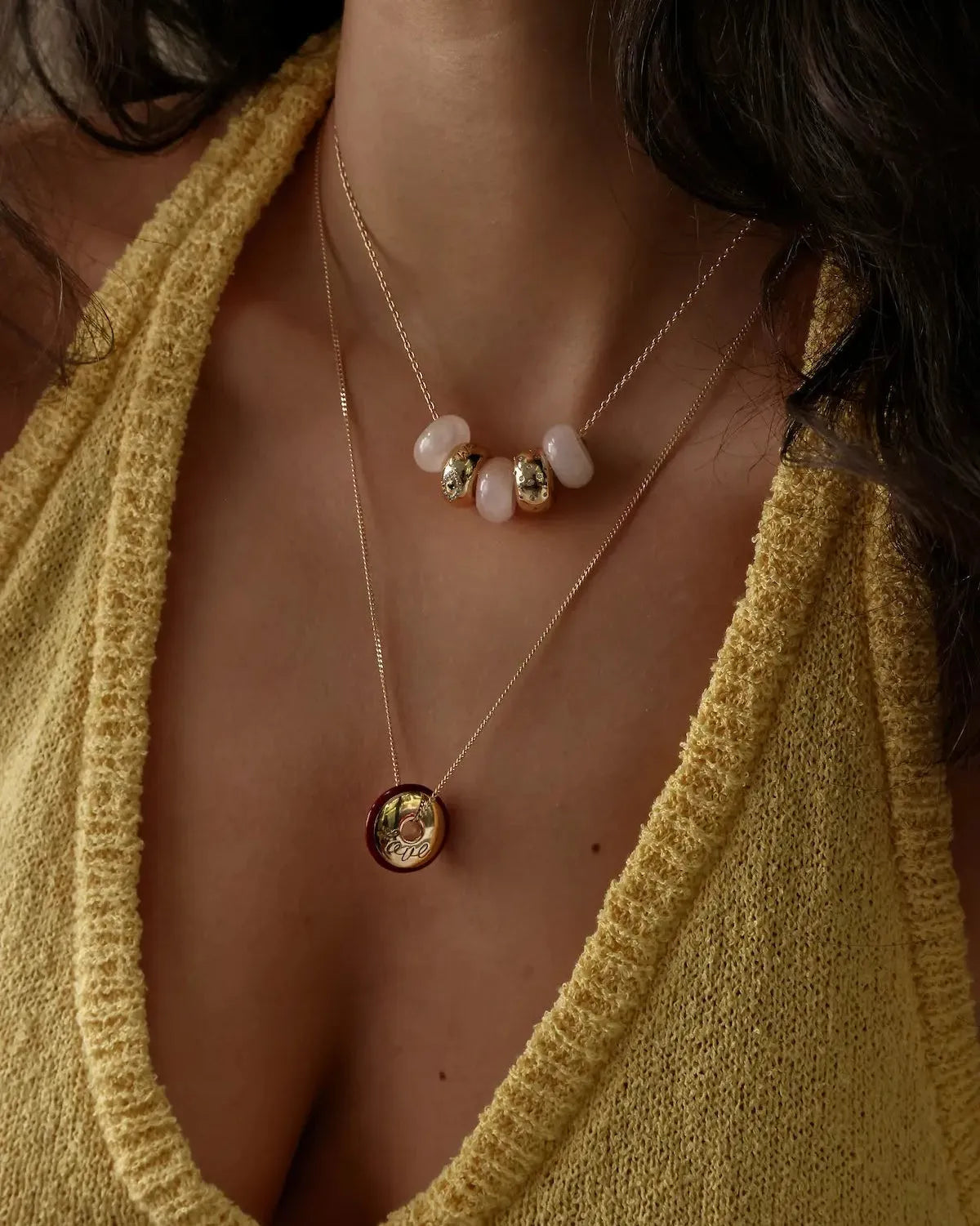 Love gold engraved necklace layered with Ava rose quartz necklace on model wearing yellow knit top, MyAleph We Are One Collection