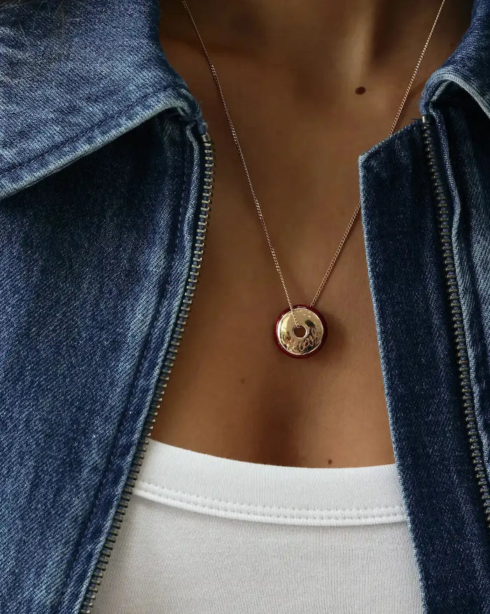 Close-up of Love gold necklace with red enamel border and love script engraving on model, MyAleph