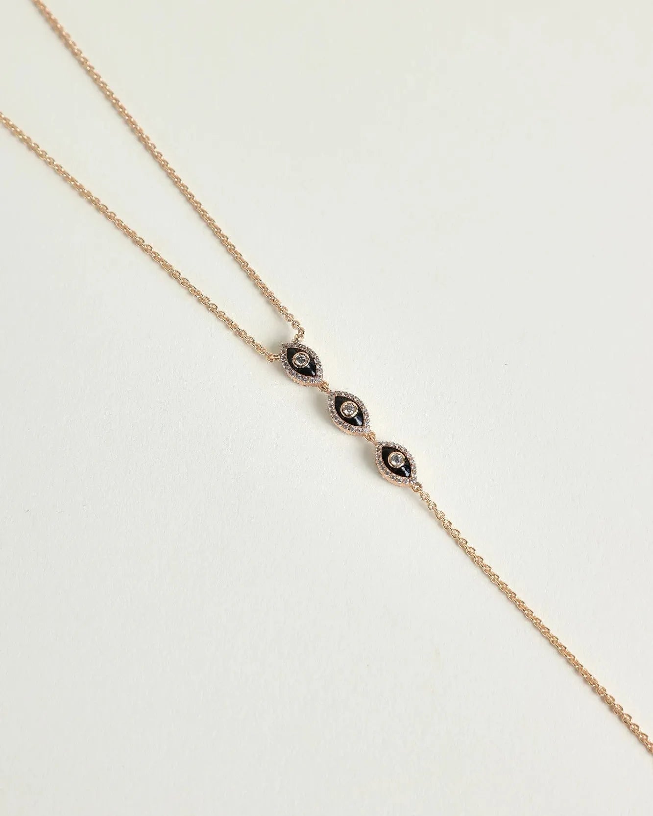 Mayra Evil Eye Body Chain in gold dipped laid flat on white surface with three black enamel evil eye charms at center