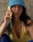 Model holding a yellow phone with the Mini Leah turquoise phone charm featuring blue beads and purple evil eye details