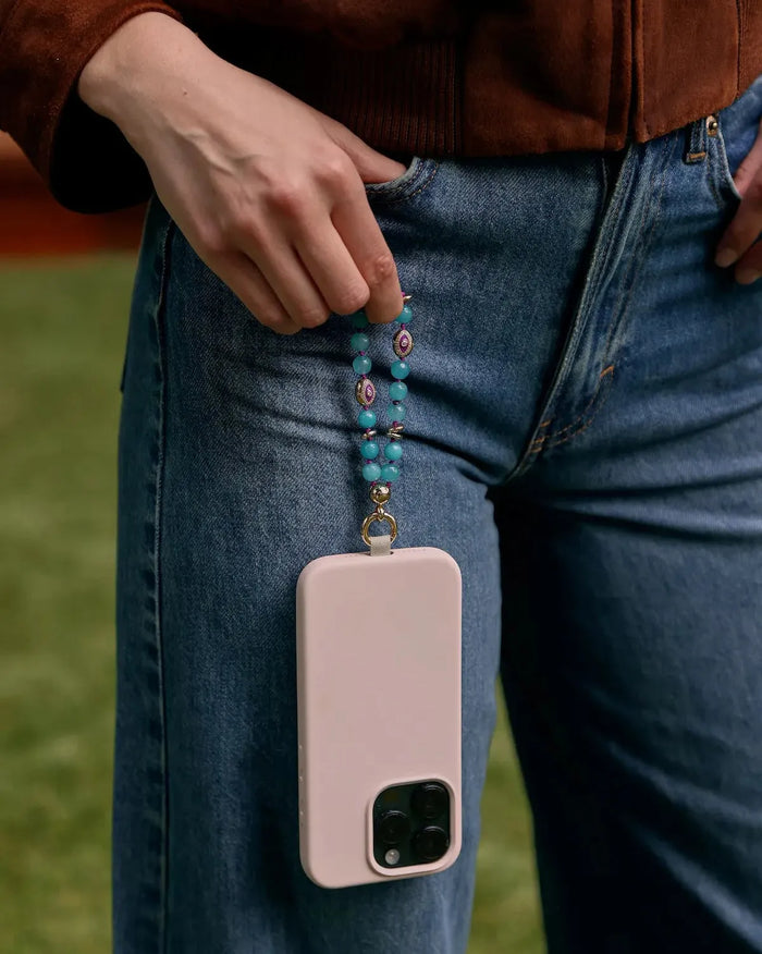 Mini Leah turquoise phone charm attached to a blush pink phone case, styled in hand against blue denim jeans