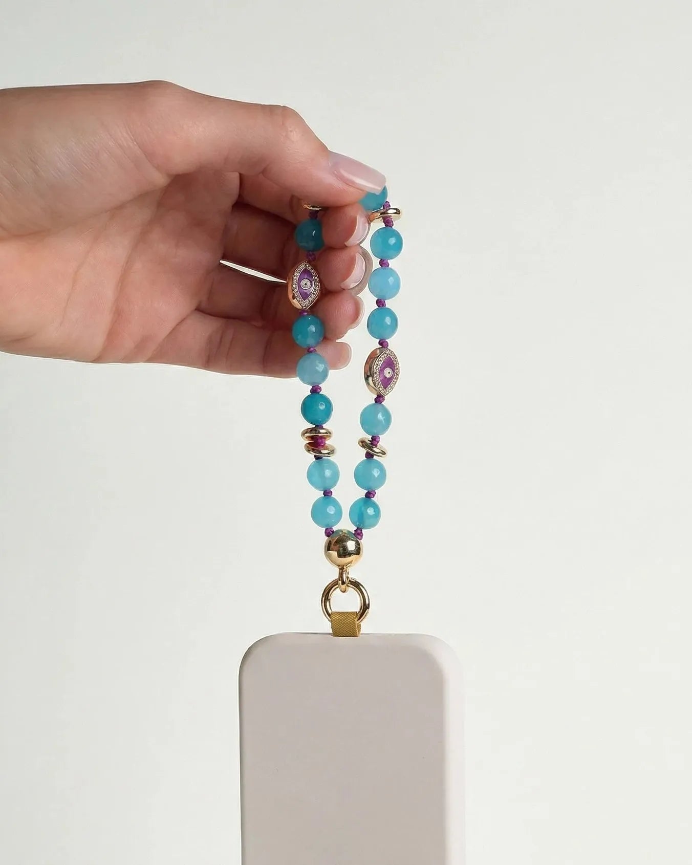 Mini Leah turquoise phone charm attached to a blush pink phone case, held in hand against a clean white background
