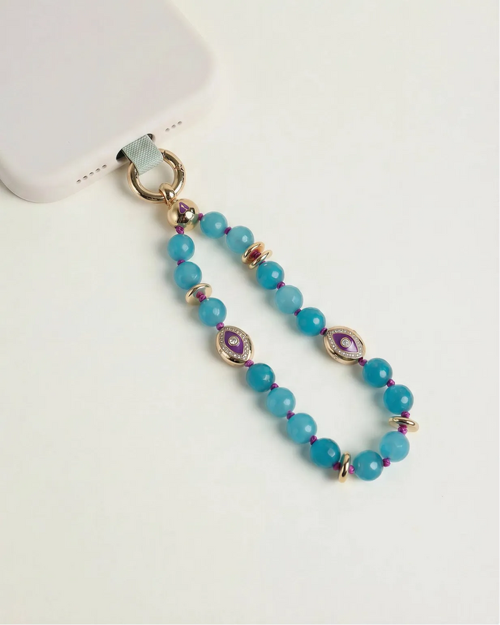 Mini Leah turquoise phone charm with blue beads, purple evil eye charms, and gold details attached to a blush pink phone case