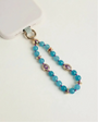 Mini Leah turquoise phone charm with blue beads, purple evil eye charms, and gold details attached to a blush pink phone case