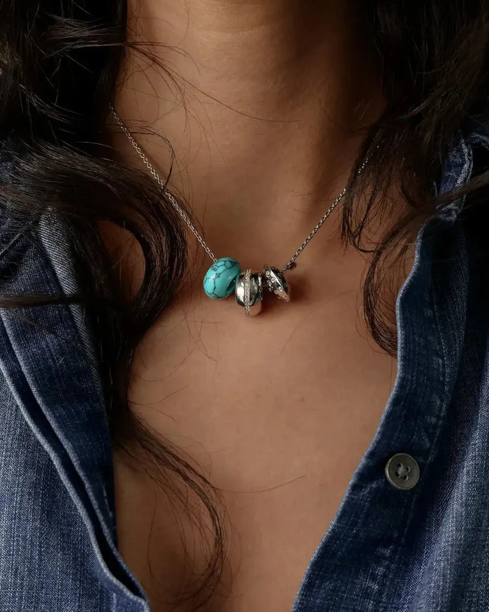 Noa silver charm necklace with turquoise bead and diamond-detailed charms styled with a denim shirt by MyAleph