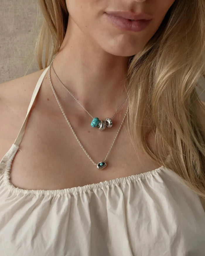 Noa silver turquoise quartz necklace layered with an evil eye pendant necklace on a white top, MyAleph We Are One Collection