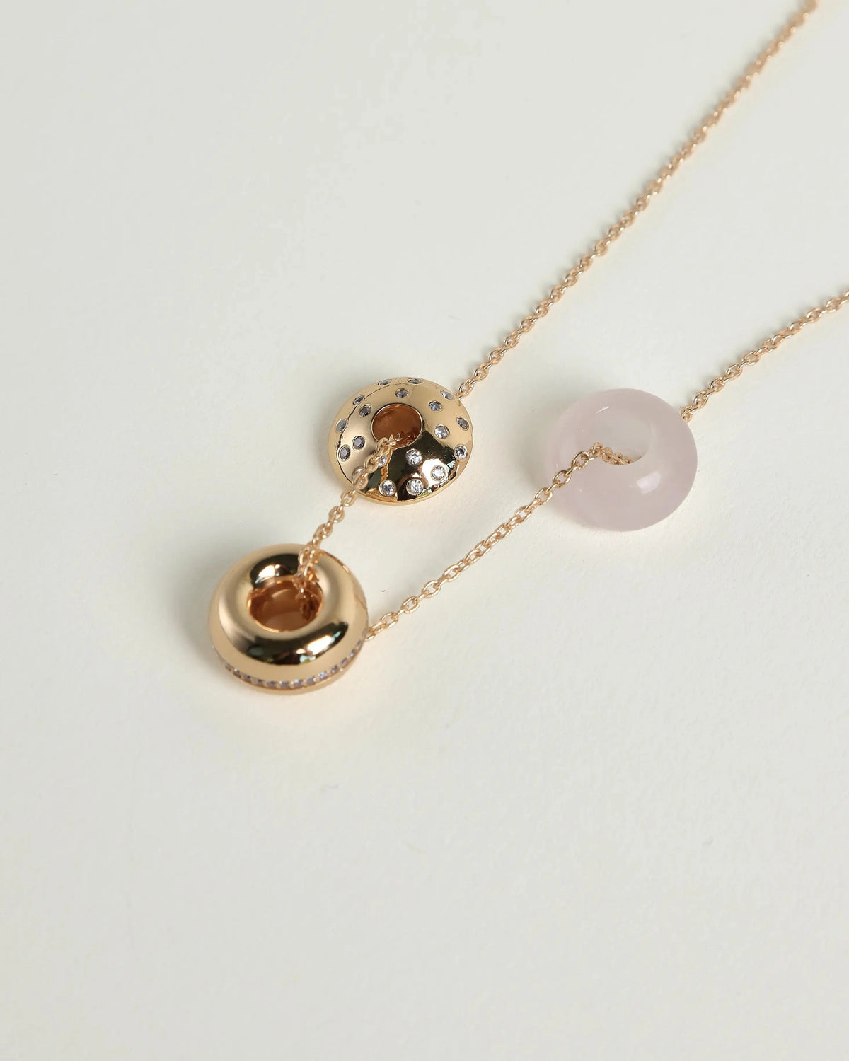 Noa Gold Necklace featuring a round rose quartz bead and two small gold-toned donut charms on a delicate 18K gold-plated chain.