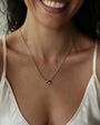 Close-up of a woman wearing a gold aura evil eye necklace with a turquoise gemstone.