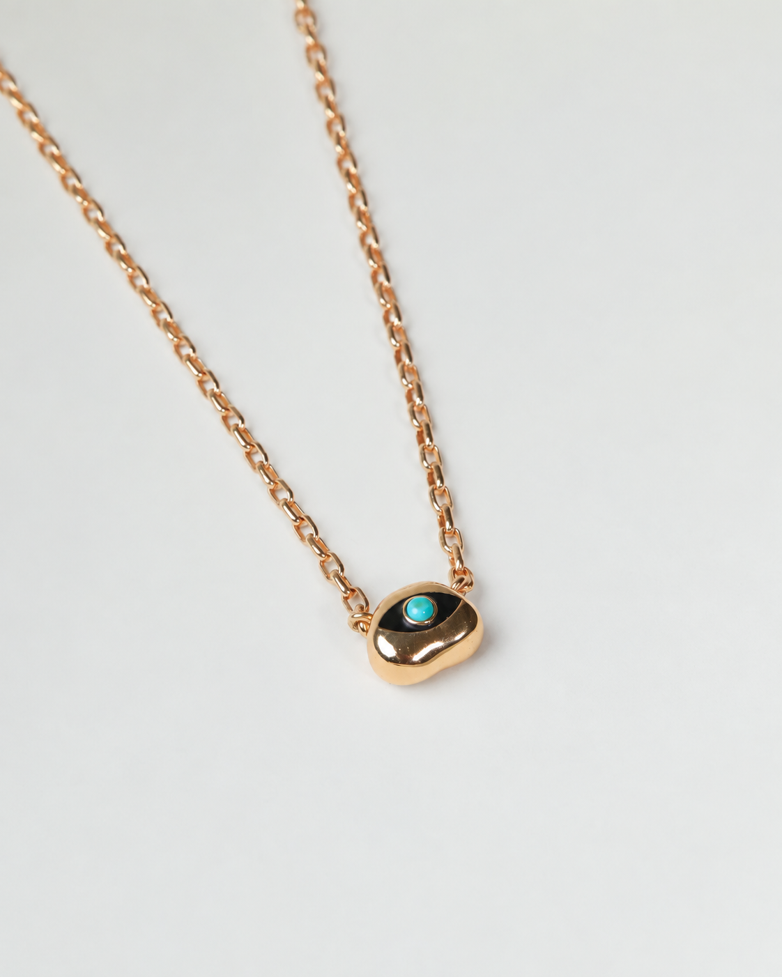 Flatlay of Gold Aura evil eye necklace with a sculptural shaped pendant with turquoise stone on a white background