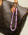 Leah Bag Charm attached to a brown monogram handbag – The lavender quartz charm clipped onto a brown leather designer bag, demonstrating its versatility and stylish appeal.